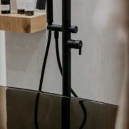 Czarna bateria wannowa, minimalistyczna półka z kosmetykami 'Au Lait', elegancka wanna. Detal projektu łazienki, nowoczesny design.