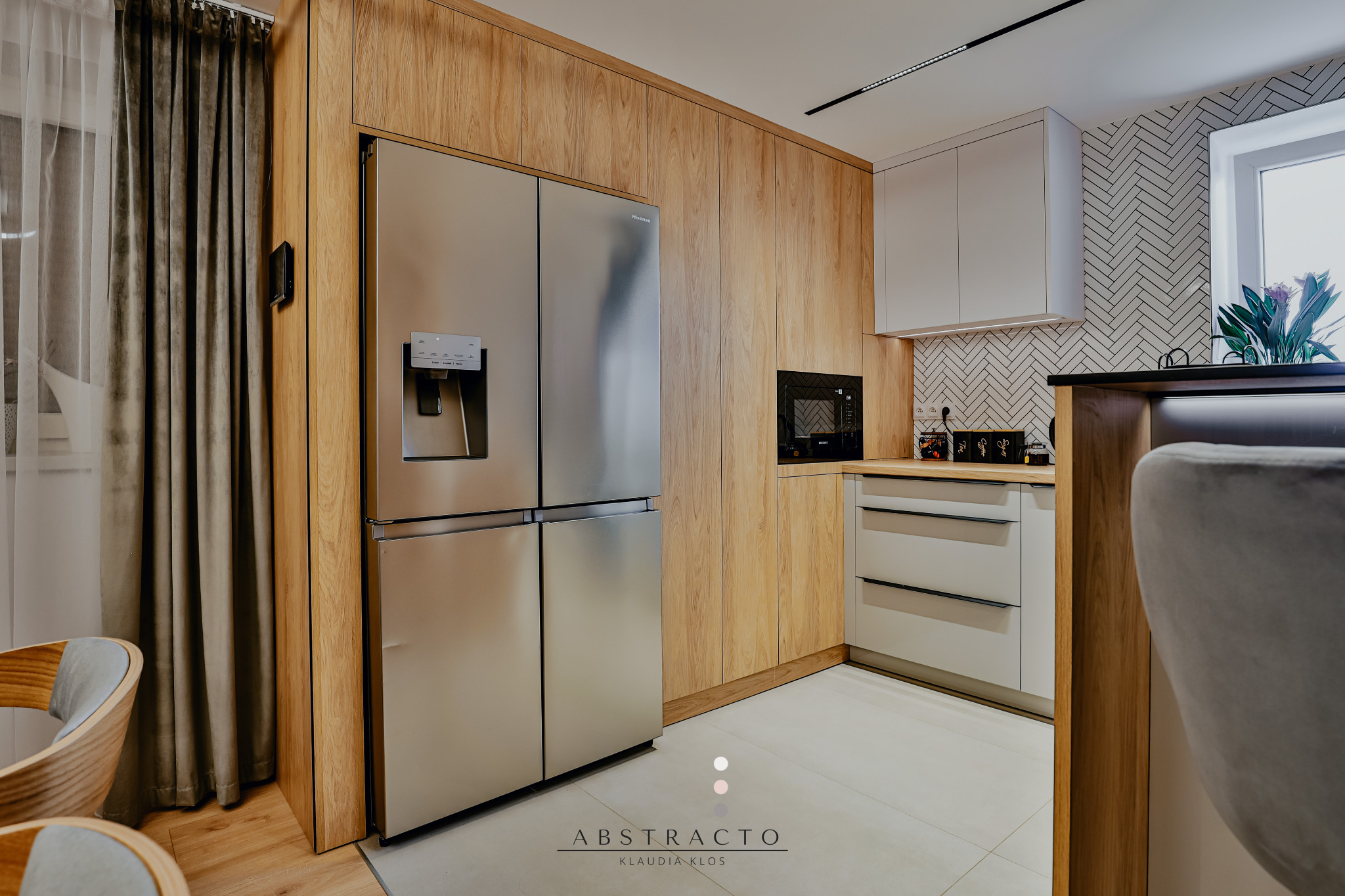 Nowoczesna kuchnia: drewniane szafki, srebrna lodówka side-by-side, białe szafki wiszące i płytki w jodełkę. Minimalistyczny design z akcentami drewna.