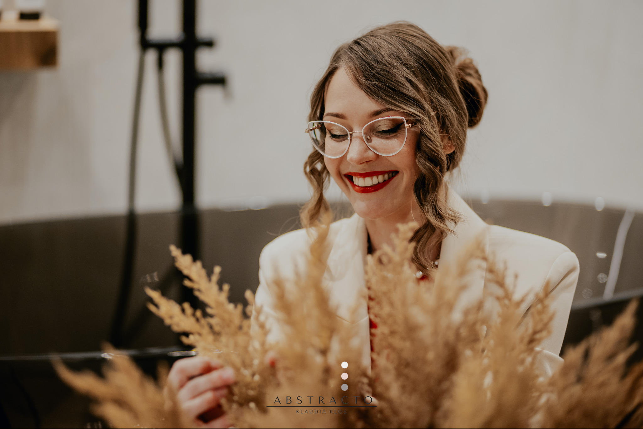 Uśmiechnięta kobieta w okularach, w jasnym wnętrzu łazienki z czarną wanną, trzymająca suszone trawy. Elegancki detal aranżacji wnętrza.