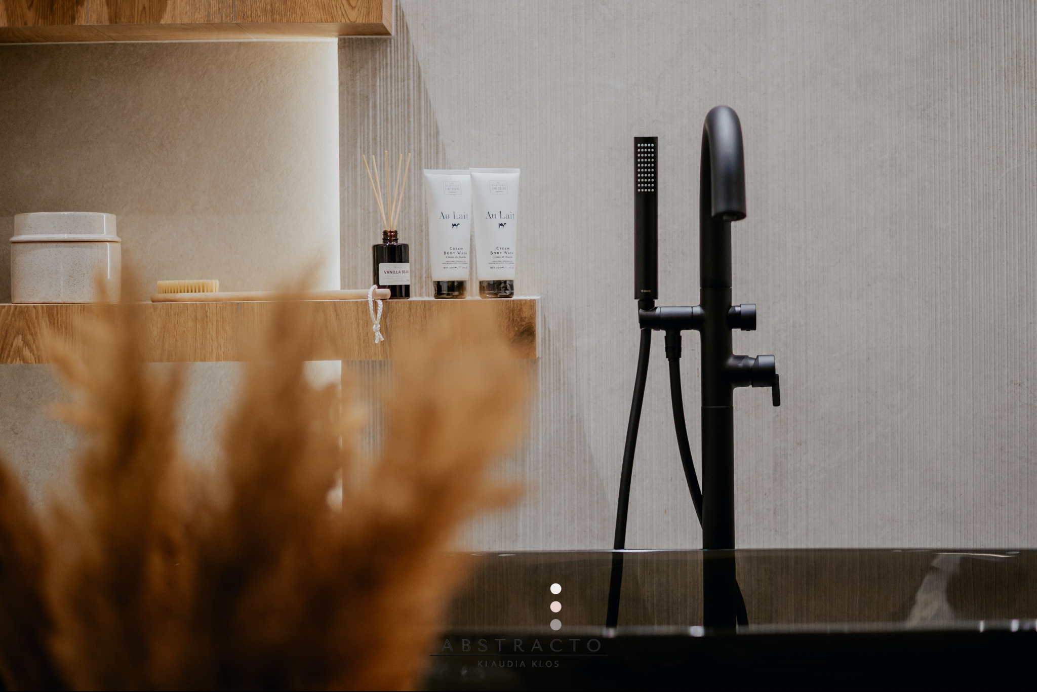 Nowoczesna łazienka z czarną armaturą, kosmetykami Au Lait na drewnianej półce i dekoracyjnymi trawami. Minimalistyczny design, stonowana kolorystyka.