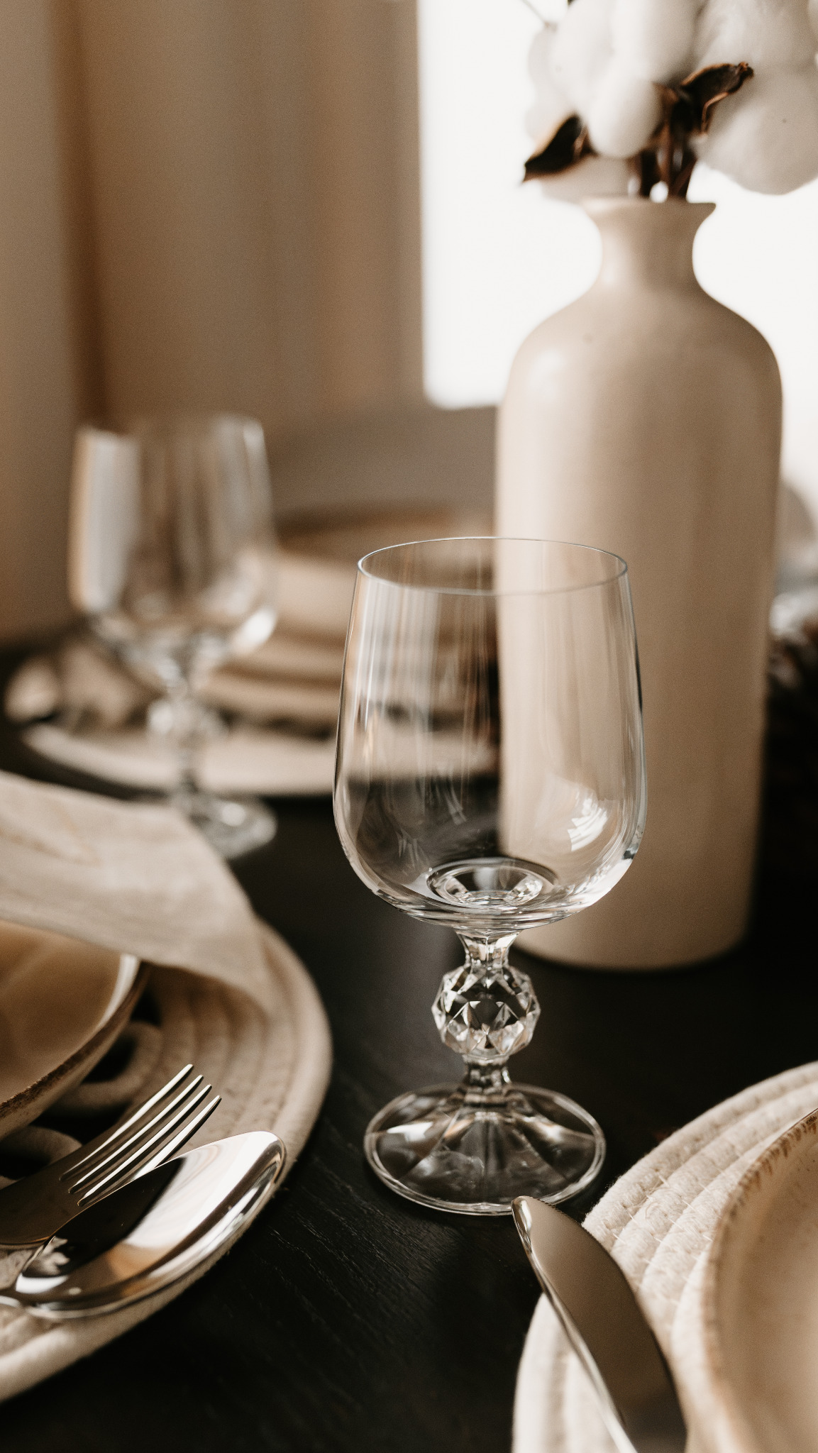 Elegancko nakryty stół z kryształowym kieliszkiem, beżową zastawą i wazonem z bawełną. Stonowana kolorystyka, minimalistyczny styl, detale podkreślają dbałość o estetykę.