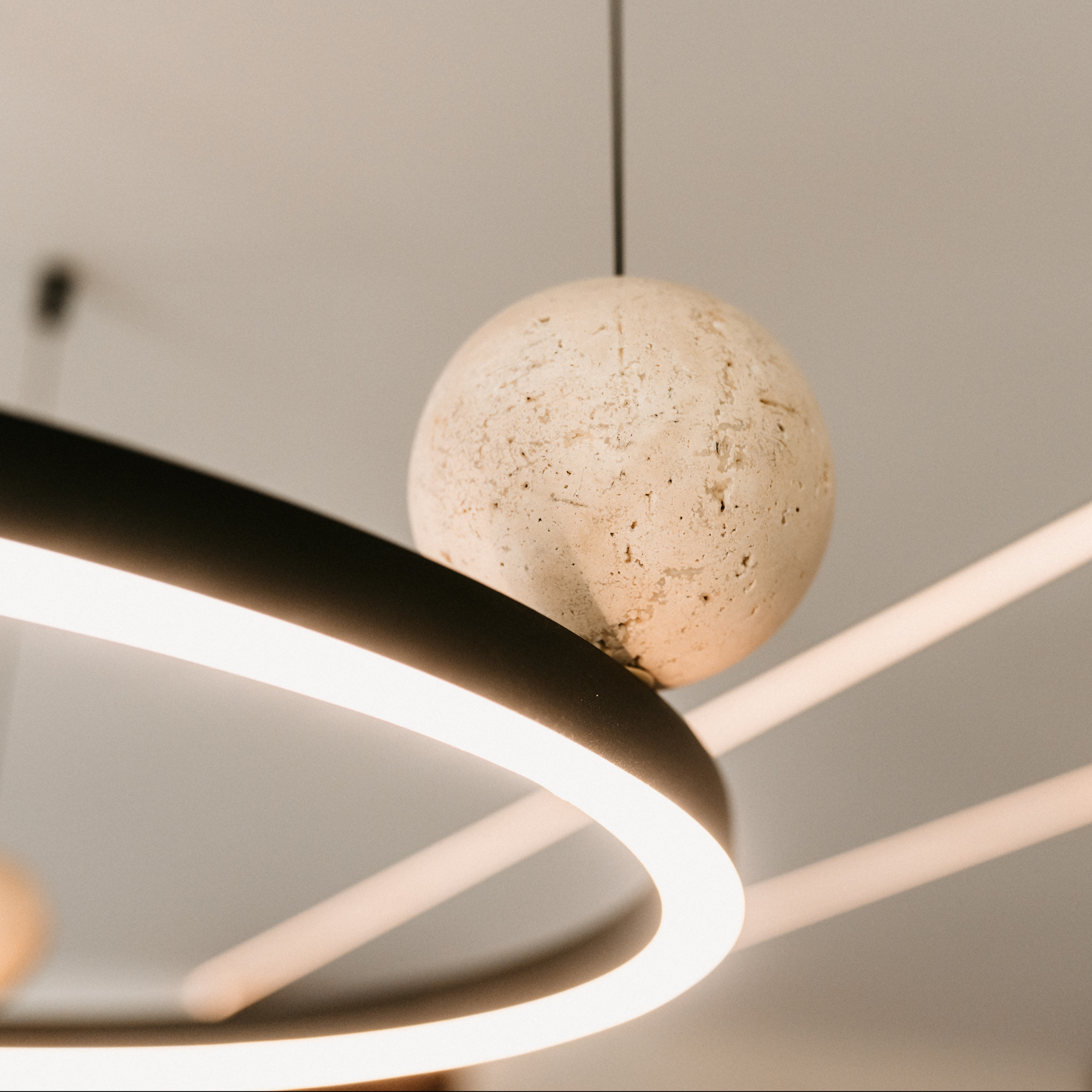 Nowoczesna lampa sufitowa z okrągłym, kamiennym kloszem i ledowym pierścieniem, oświetlająca wnętrze ciepłym światłem. Minimalistyczny design.