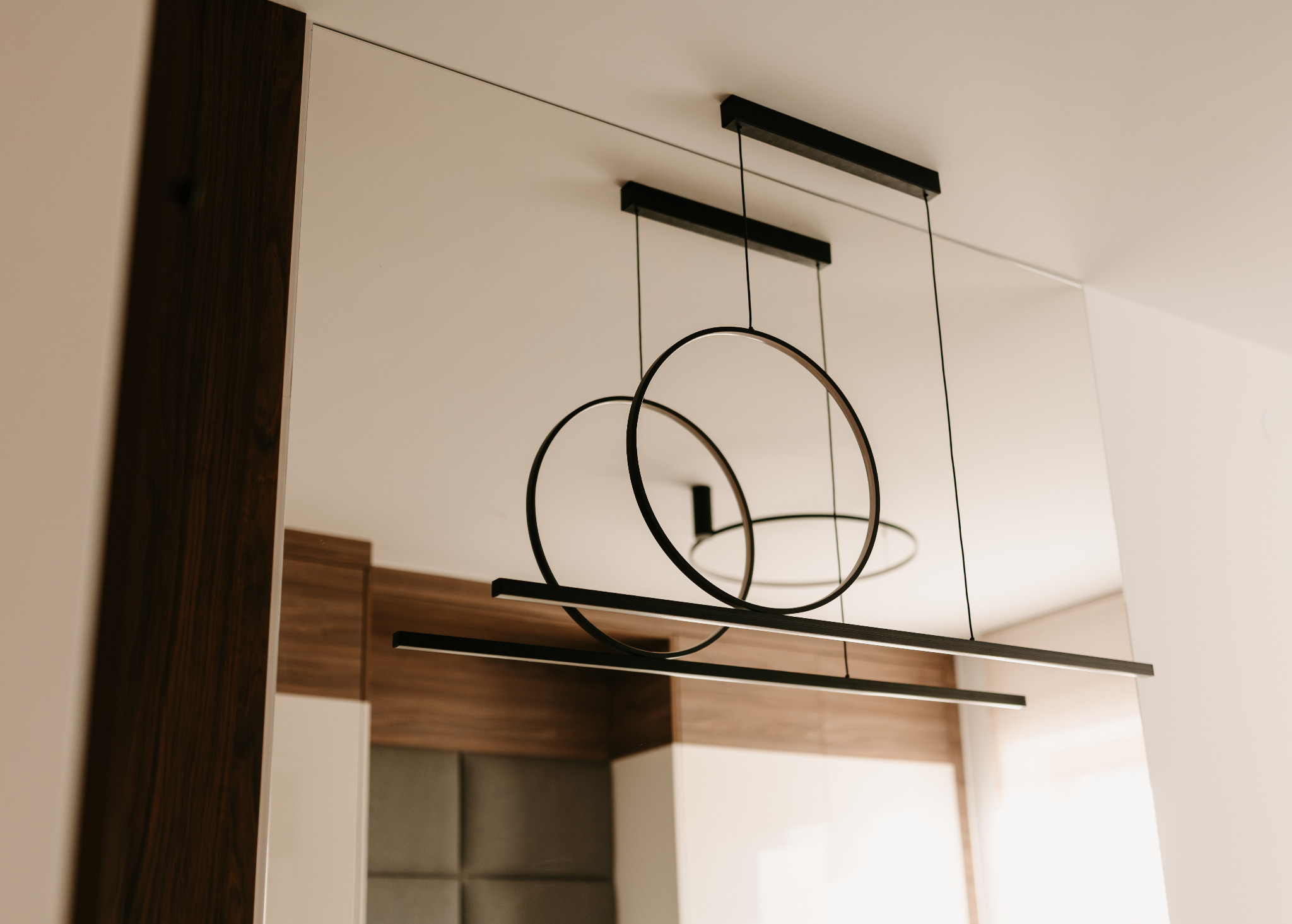 Nowoczesna lampa wisząca z okrągłymi i prostokątnymi elementami w minimalistycznym wnętrzu, odbicie zabudowy meblowej. Usługi w Rabce-Zdroju.