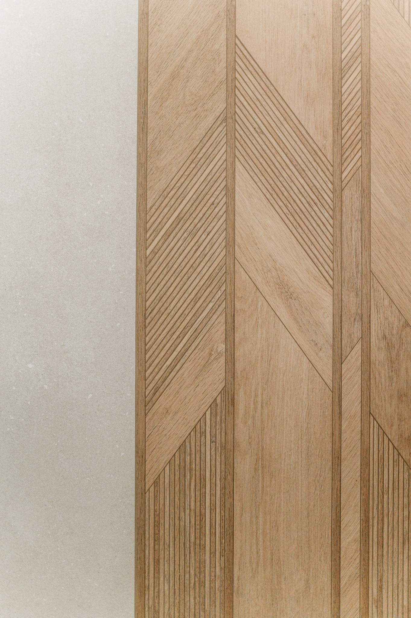Drewniana okładzina ścienna z geometrycznym wzorem jodełki, sąsiadująca z jasną, gładką powierzchnią. Detal wykończenia wnętrza w neutralnej kolorystyce.