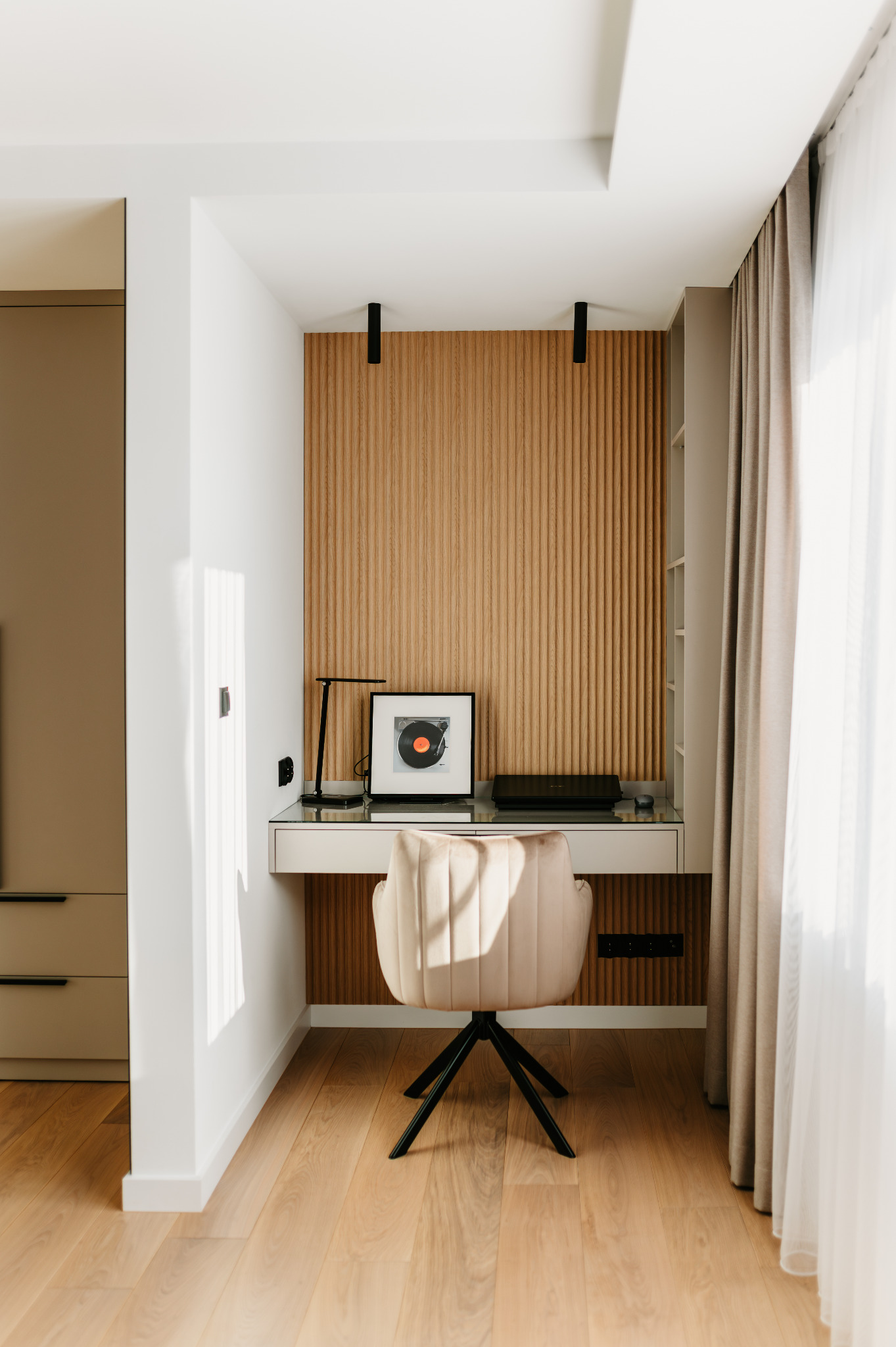 Nowoczesny kącik do pracy w domu: biurko z beżowym krzesłem na tle drewnianej ściany z pionowymi panelami. Na biurku lampka i grafika z płytą winylową.