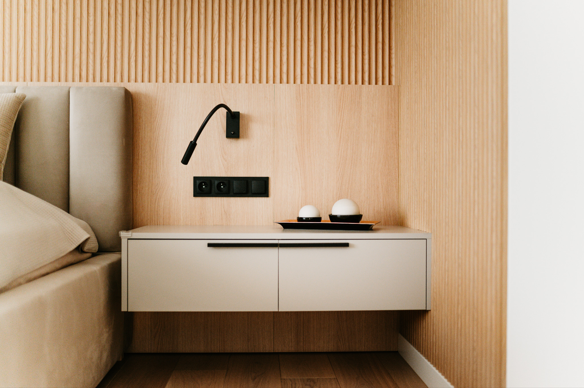 Minimalistyczna sypialnia: beżowe panele ścienne, szafka nocna z lampką i dekoracjami. Subtelne oświetlenie, jasne kolory, nowoczesny design.