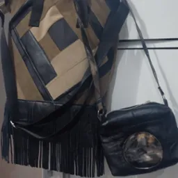 Dwie torebki damskie: duża patchworkowa z frędzlami i mała czarna z okrągłym elementem, wiszące na białej szafie.