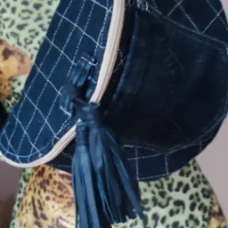 Czarna, pikowana kosmetyczka z zamkiem błyskawicznym i skórzanymi frędzlami, wisząca na manekinie w panterkę.