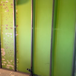 Prywatnie - Montaż stelaża z profili metalowych do płyty G-K na ścianie w odcieniach zieleni. W tle widoczny fragment ściany z resztkami farby. Na podłodze leży wkrętarka.