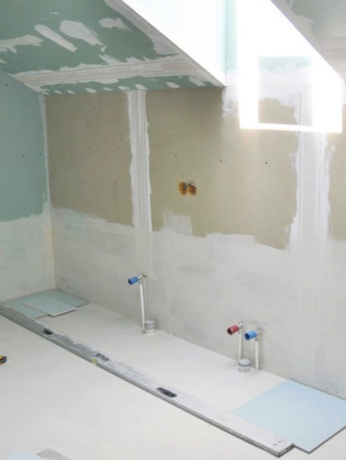 Łazienka w trakcie prac wykończeniowych: ściany z płyt gipsowo-kartonowych, poziomica na podłodze, przygotowane przyłącza wodne. Widoczne etapy prac.