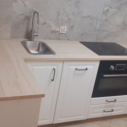 APOLLO ANDRII ZINCHENKO - Jasna kuchnia z białymi szafkami, drewnianym blatem i marmurową ścianą nad blatem, w rogu widoczny zlew i płyta indukcyjna.