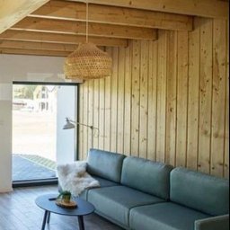 APOLLO ANDRII ZINCHENKO - Jasne drewno na suficie i ścianach tworzy ciepły kontrast z turkusową sofą. Wnętrze dopełnia pleciona lampa i minimalistyczny stolik kawowy.