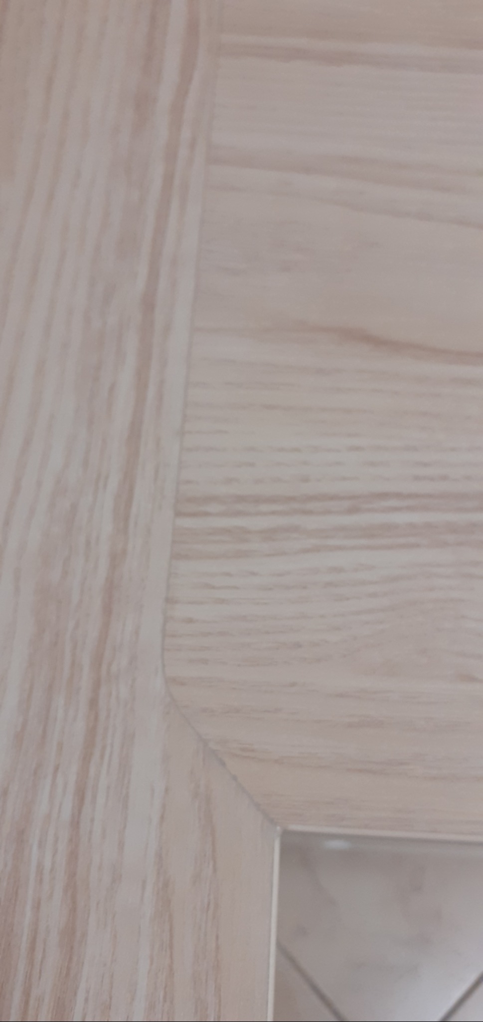 Fragment podłogi wyłożonej panelami w odcieniach jasnego drewna, widoczny narożnik z zaokrąglonym brzegiem i fragment płytek podłogowych w tle.