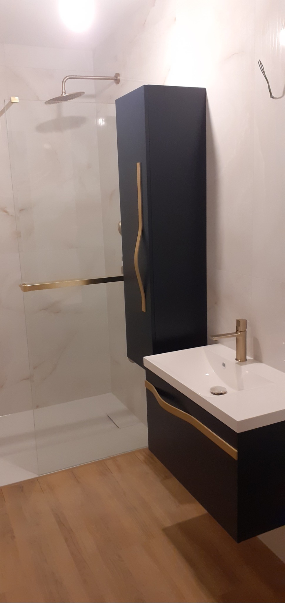 Nowoczesna łazienka z kabiną prysznicową typu walk-in, szafką umywalkową w kolorze granatowym z elementami w kolorze złota i białą umywalką.