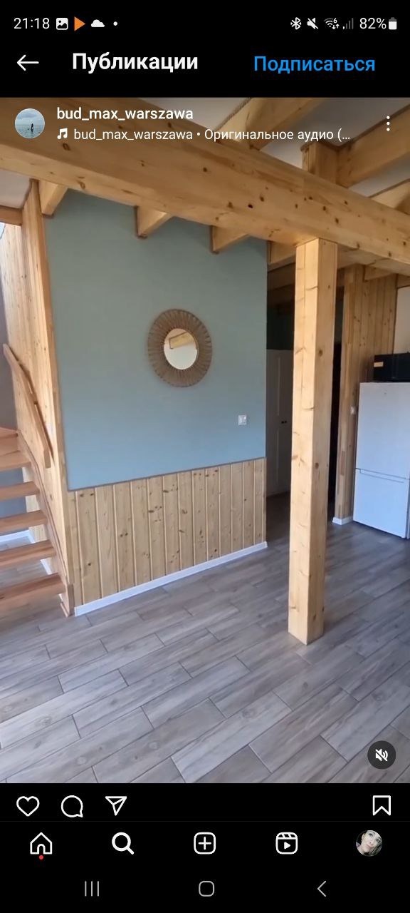 Wykończenie wnętrza: drewniane panele ścienne, szare płytki podłogowe, drewniane schody i strop, okrągłe lustro na niebieskiej ścianie. Nowoczesny design.