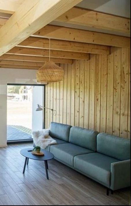 Jasne drewno na suficie i ścianach tworzy ciepły kontrast z turkusową sofą. Wnętrze dopełnia pleciona lampa i minimalistyczny stolik kawowy.