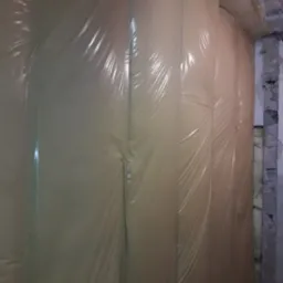 Ściana wewnętrzna ocieplona wełną mineralną i folią paroizolacyjną, widoczne fragmenty surowego muru i instalacji pod sufitem.
