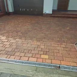 Ułożona kostka brukowa w odcieniach czerwieni i żółci na podjeździe w Nysie, z widocznym odpływem liniowym i fragmentem elewacji domu z garażem.