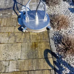 Profesjonalna maszyna czyszcząca z okrągłą głowicą w trakcie pracy na kostce brukowej, widoczny efekt czyszczenia, zarys cienia osoby obsługującej sprzęt.