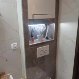 Nowoczesna łazienka z marmurowymi płytkami, podświetlaną wnęką z dekoracjami zapachowymi i minimalistyczną armaturą.