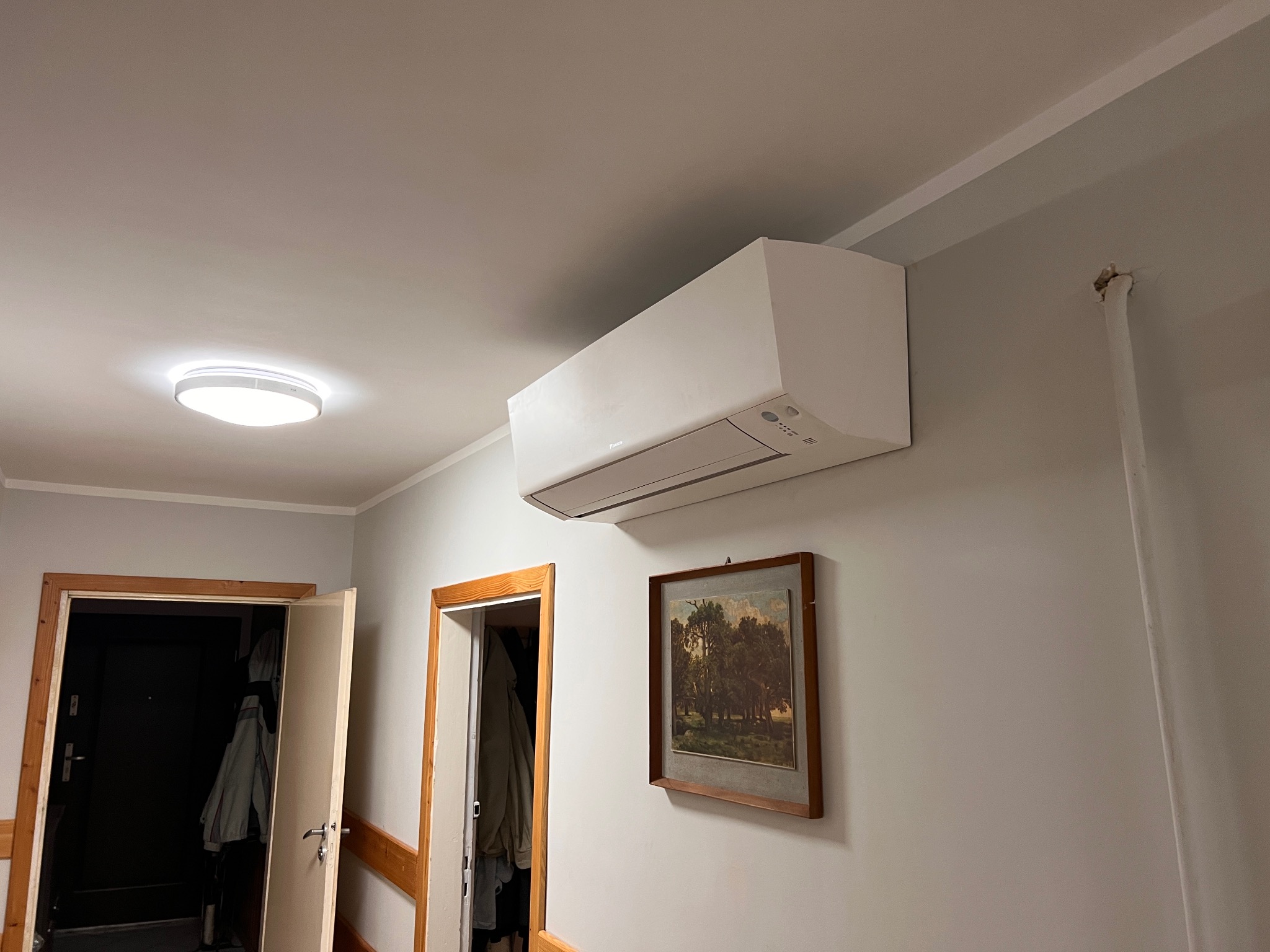 Zamontowana jednostka klimatyzacji Daikin na ścianie w mieszkaniu w Olsztynie, widoczny obrazek w ramie i otwarte drzwi do innego pomieszczenia.