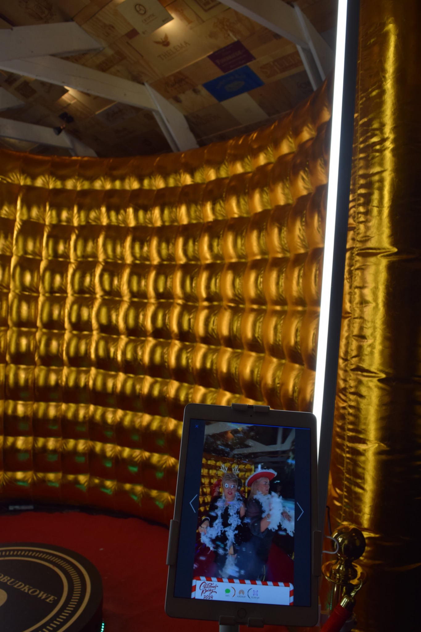 Złota, dmuchana ściana fotobudki z oświetleniem LED, na pierwszym planie tablet wyświetlający zdjęcie dwóch kobiet w przebraniach z rekwizytami.
