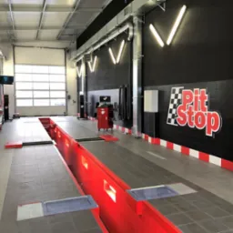 Wnętrze warsztatu samochodowego z kanałem inspekcyjnym, wyposażone w nowoczesny sprzęt diagnostyczny i oświetlenie LED, z logo 'Pit Stop' na czarnej ścianie.