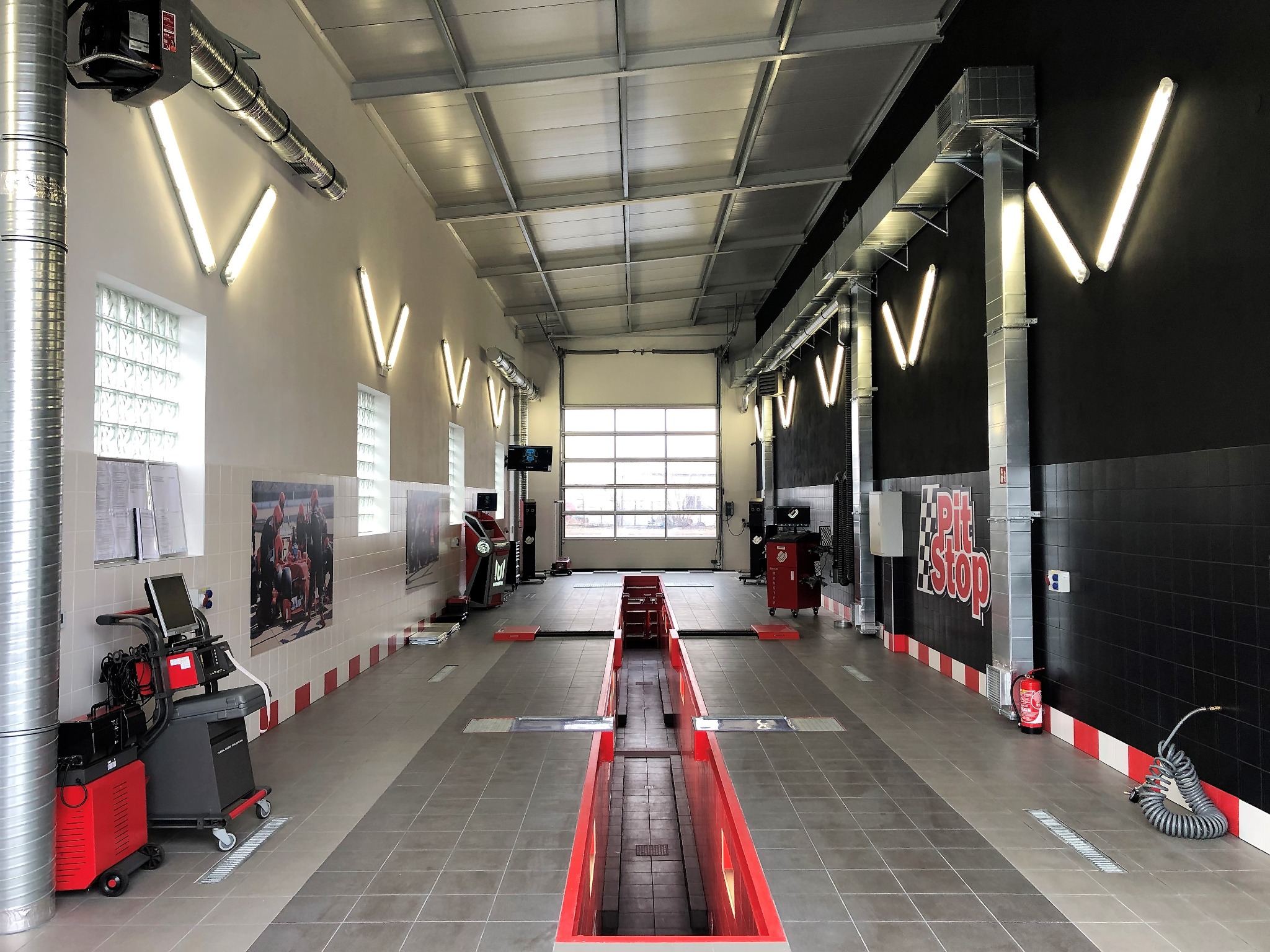 Wnętrze nowoczesnego warsztatu samochodowego z kanałem naprawczym, oświetleniem w kształcie litery V na ścianach i napisem 'Pit Stop'.