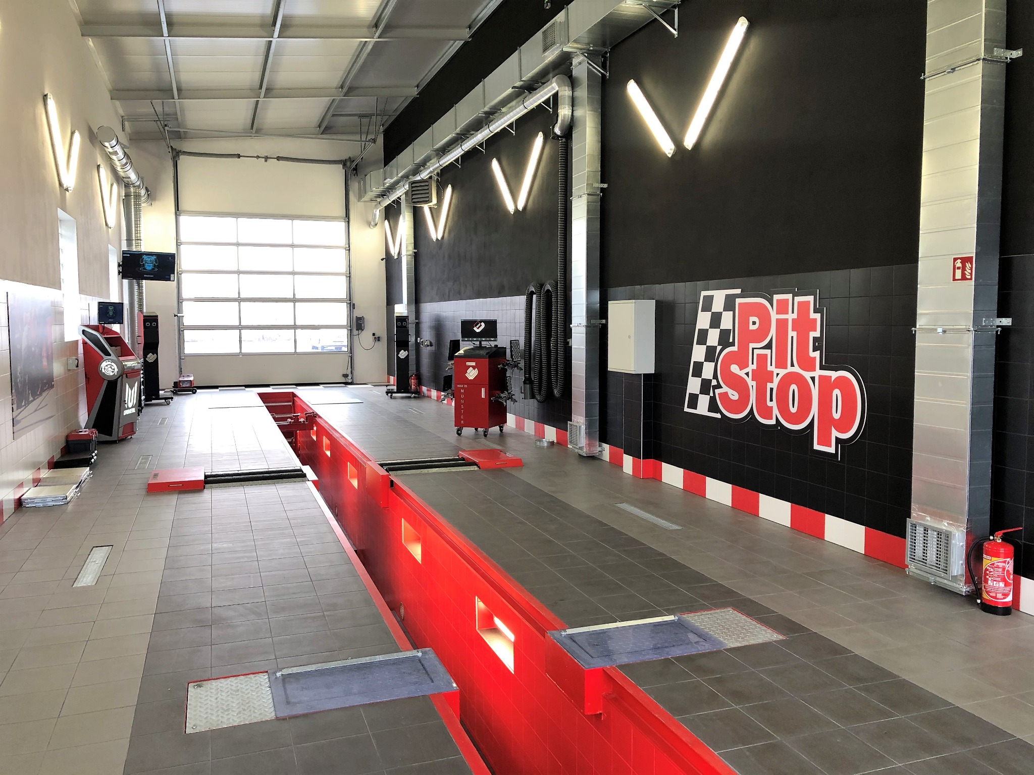 Wnętrze warsztatu samochodowego z kanałem inspekcyjnym, wyposażone w nowoczesny sprzęt diagnostyczny i oświetlenie LED, z logo 'Pit Stop' na czarnej ścianie.
