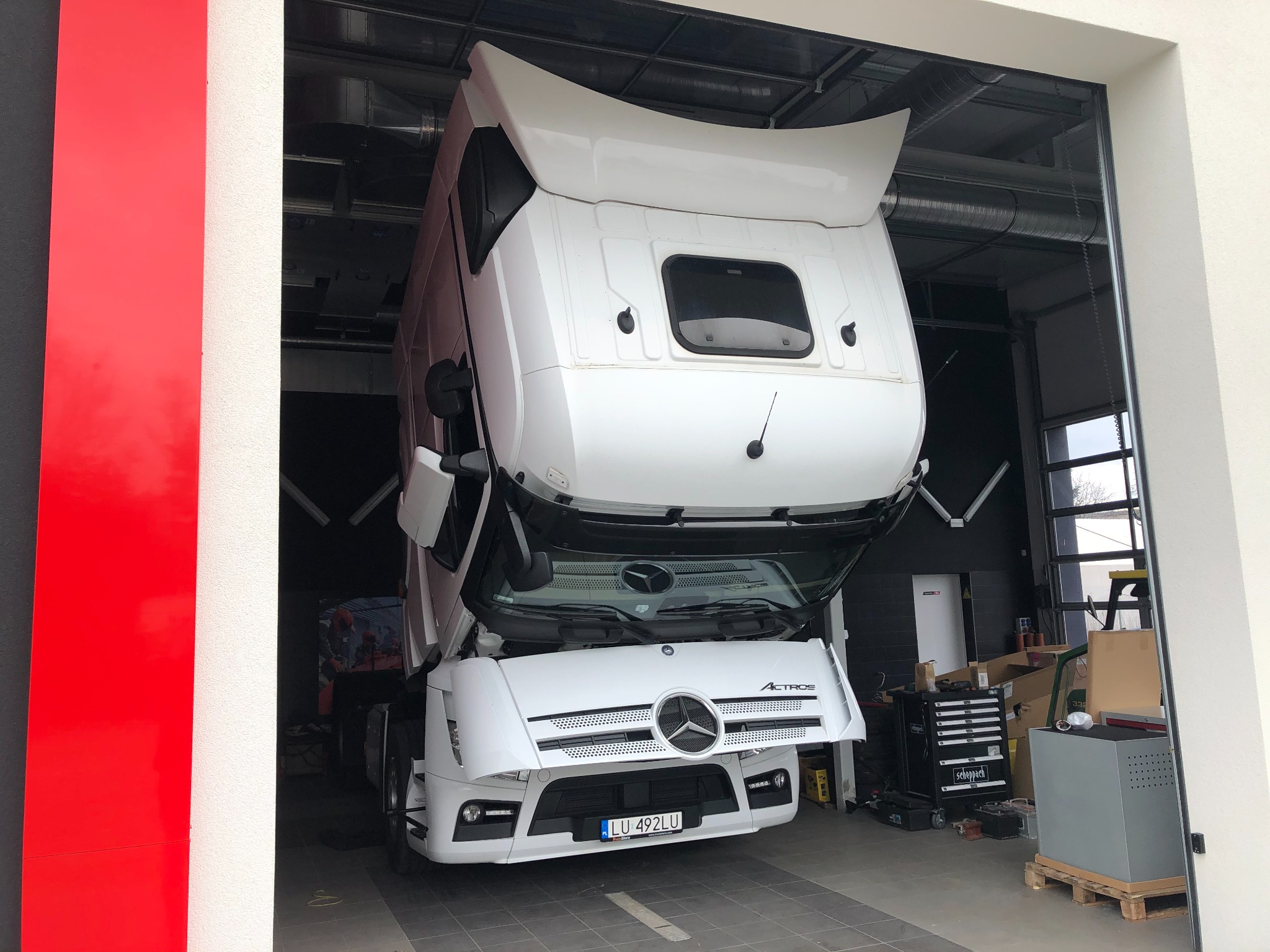 Biały ciągnik siodłowy Mercedes Actros z podniesioną kabiną w warsztacie, widoczny numer rejestracyjny LU 492LU, skrzynka z narzędziami Scheppach w tle.