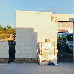 VANBUD - Wznoszenie ścian domu z betonu komórkowego, widoczne pustaki i zaplecze budowy z samochodem w tle, wczesna faza budowy domu.