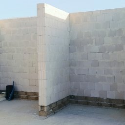 VANBUD - Wnętrze budynku w trakcie budowy: ściany z białych bloczków, widoczny fundament. Częściowo wzniesione ściany działowe. Niski kąt ujęcia podkreśla surowość stanu deweloperskiego.