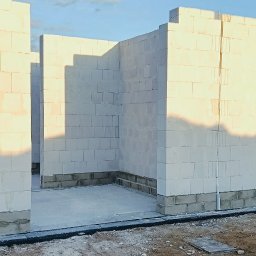VANBUD - Wnętrze domu w trakcie budowy: ściany z białych bloczków, widoczne fundamenty i częściowe oświetlenie słoneczne. Surowy stan, przygotowanie do dalszych prac.
