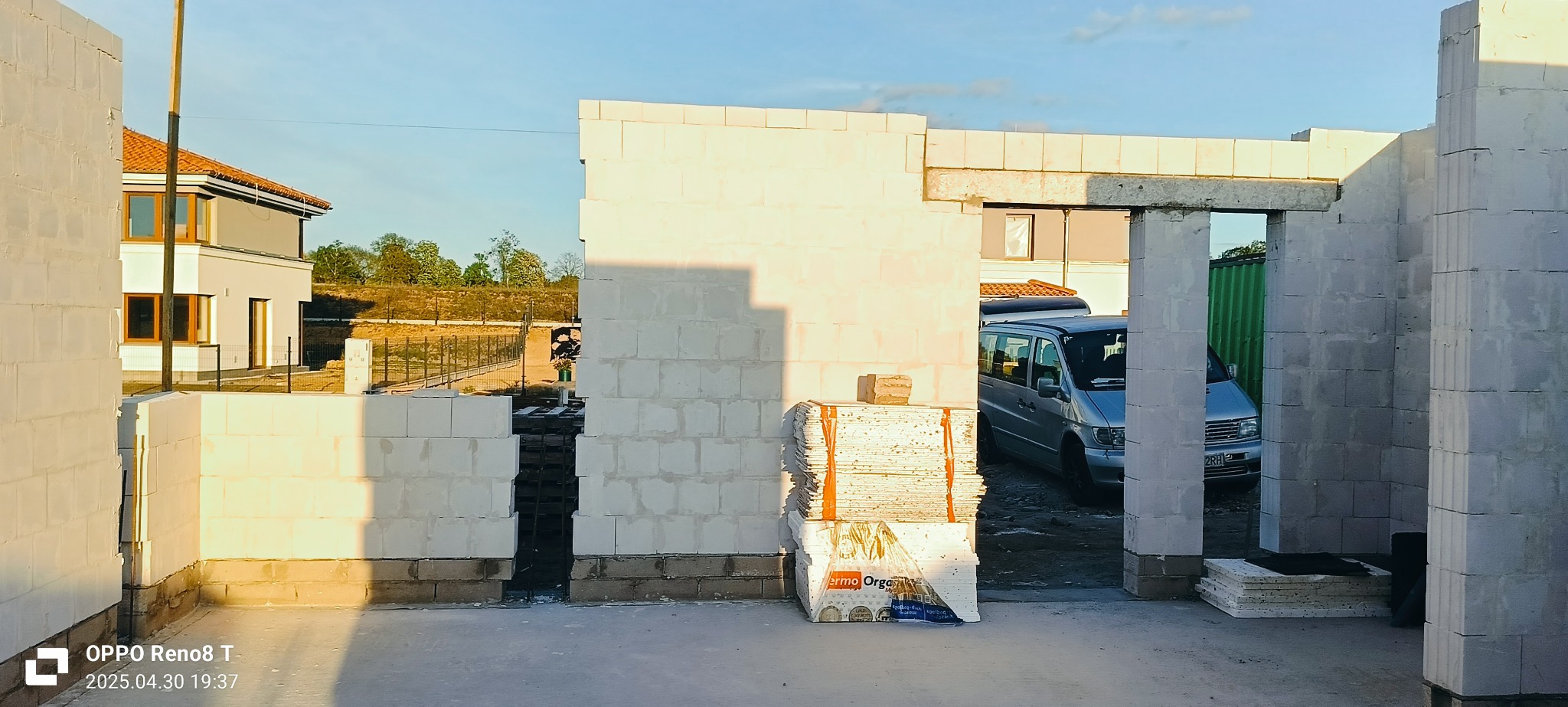 Wznoszenie ścian domu z betonu komórkowego, widoczne pustaki i zaplecze budowy z samochodem w tle, wczesna faza budowy domu.