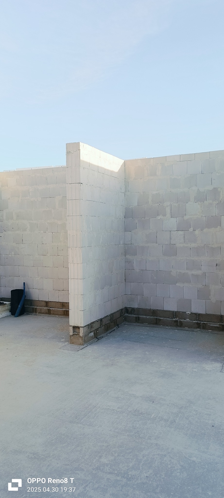 Wnętrze budynku w trakcie budowy: ściany z białych bloczków, widoczny fundament. Częściowo wzniesione ściany działowe. Niski kąt ujęcia podkreśla surowość stanu deweloperskiego.