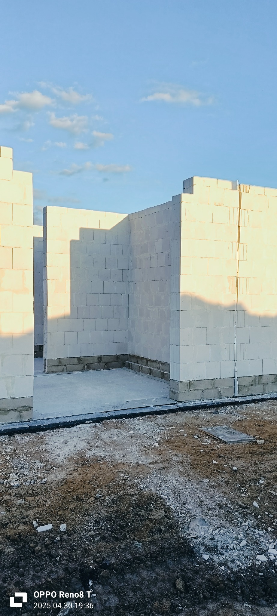 Wnętrze domu w trakcie budowy: ściany z białych bloczków, widoczne fundamenty i częściowe oświetlenie słoneczne. Surowy stan, przygotowanie do dalszych prac.