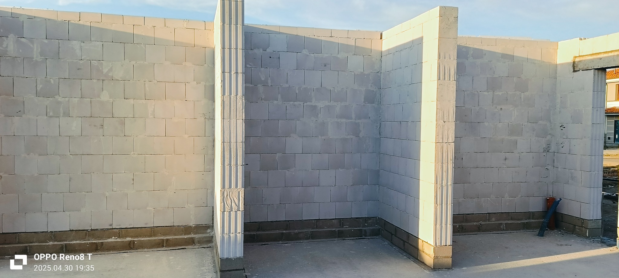 Wewnętrzne ściany z betonu komórkowego w surowym stanie, widoczne charakterystyczne pionowe żłobienia na narożnikach. Częściowo w cieniu, z niską podmurówką.