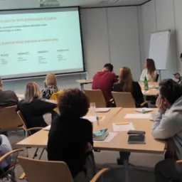 Prelegent w szarej marynarce prowadzi szkolenie z digital marketingu, prezentacja na ekranie z modelem 5P, uczestnicy siedzą przy stołach.