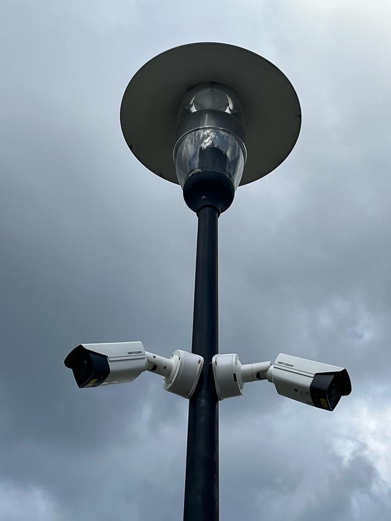 Dwie kamery monitoringu Hikvision zamontowane symetrycznie na słupie oświetleniowym, widok z dołu na tle pochmurnego nieba.