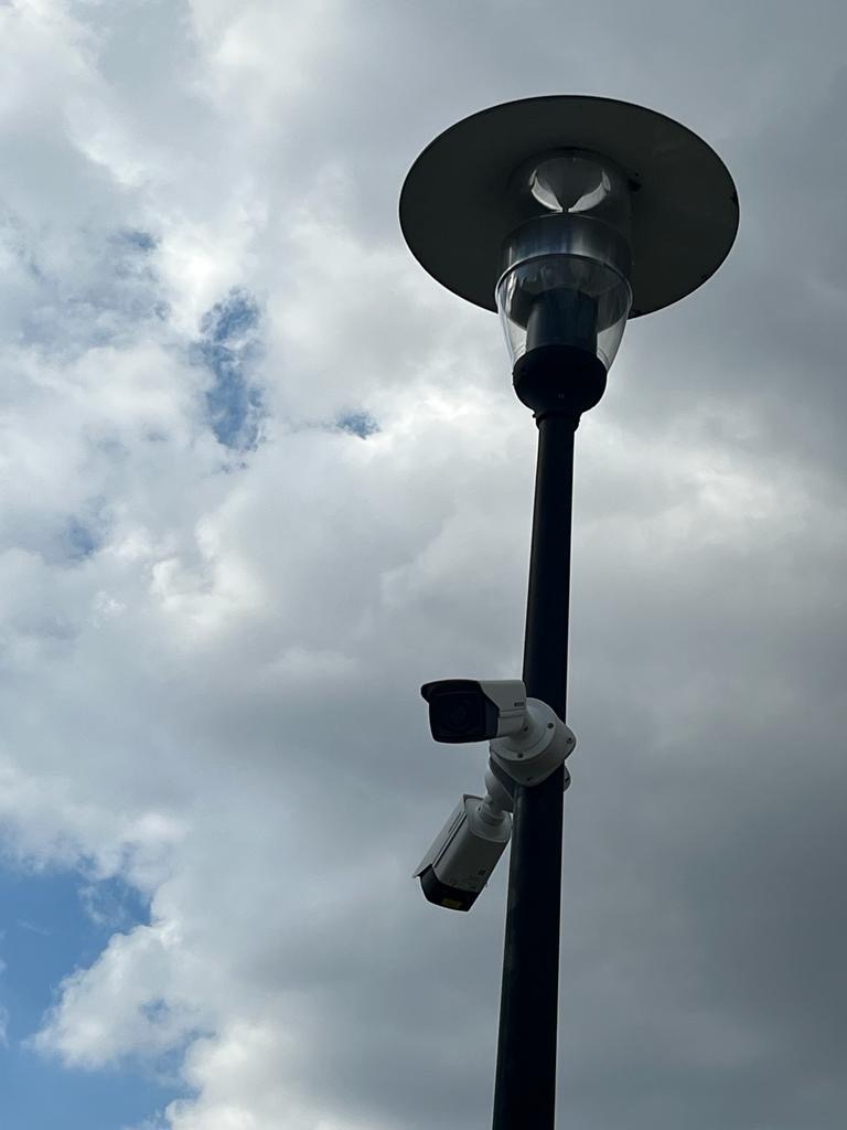 Dwie kamery monitoringu zamontowane na słupie oświetleniowym w Szczytnie, skierowane w różnych kierunkach, na tle pochmurnego nieba.