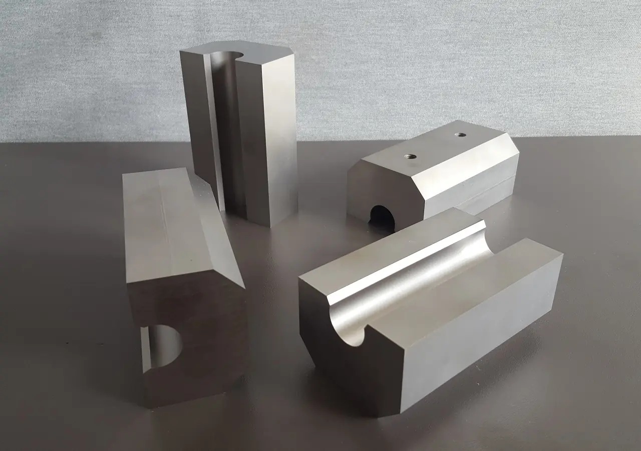 Precyzyjnie obrobione, metalowe elementy o różnych kształtach, widoczne ślady obróbki skrawaniem, ustawione na szarym blacie w neutralnym oświetleniu.