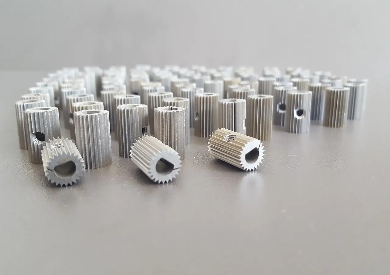 Partia srebrnych, precyzyjnie wykonanych metalowych kół zębatych z otworem i rowkiem, ułożonych na gładkiej powierzchni w równym oświetleniu.