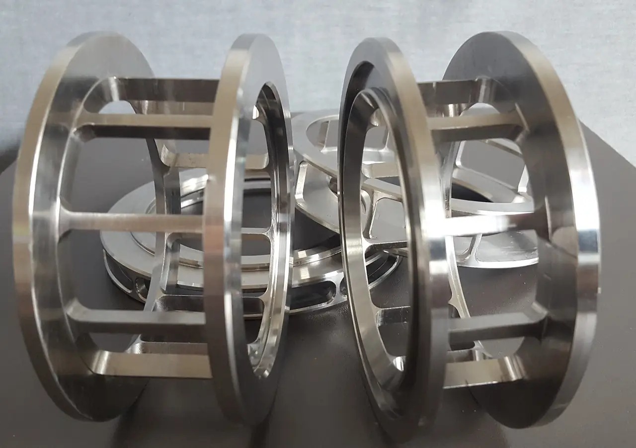 Precyzyjnie wykonane, metalowe elementy cylindryczne z otworami, prawdopodobnie komponenty maszyn, ułożone na ciemnej powierzchni, widoczne ślady obróbki.