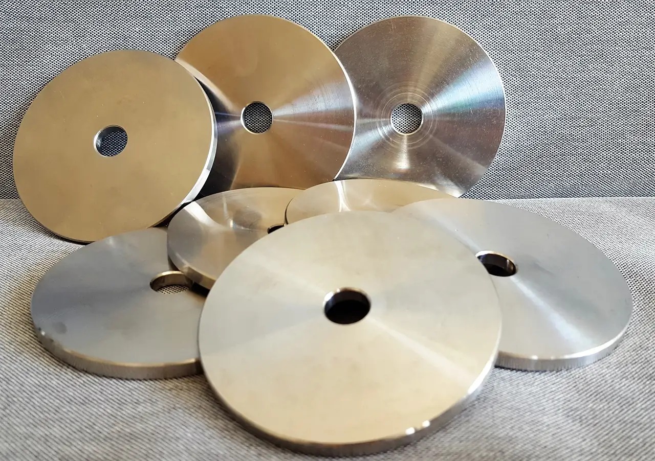 Stalowe, okrągłe elementy z centralnym otworem, ułożone na szarym, teksturowanym tle, prezentujące obróbkę metalu CNC.