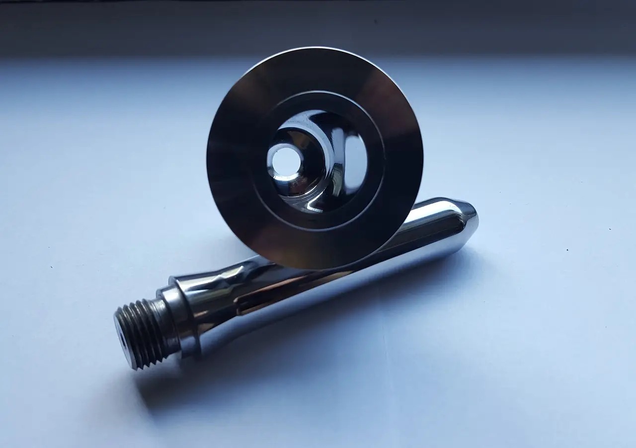 Precyzyjnie wykonany, polerowany metalowy element z gwintem i okrągłym kołnierzem, leżący na jasnym tle.