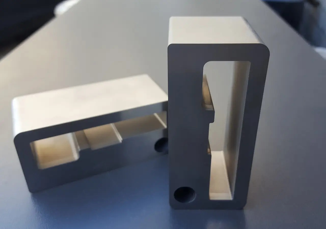 Dwa metalowe elementy z precyzyjnie wyciętymi otworami i zaokrąglonymi krawędziami, leżące na gładkiej powierzchni, ukazujące dokładność obróbki.