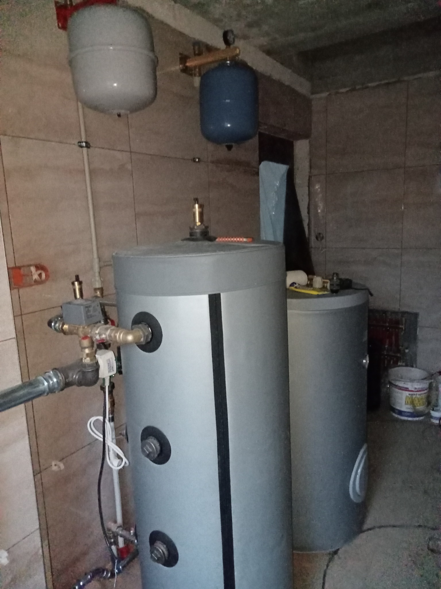 Dwa zbiorniki akumulacyjne, podłączone rurami i zaworami, zainstalowane w pomieszczeniu w Kielcach. Nad nimi widoczne naczynia wzbiorcze. Na ścianach płytki.