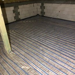 Berben - Niebieskie rurki ogrzewania podłogowego ułożone na siatce w surowym wnętrzu poddasza z ociepleniem stropu i ścianami z betonu komórkowego.