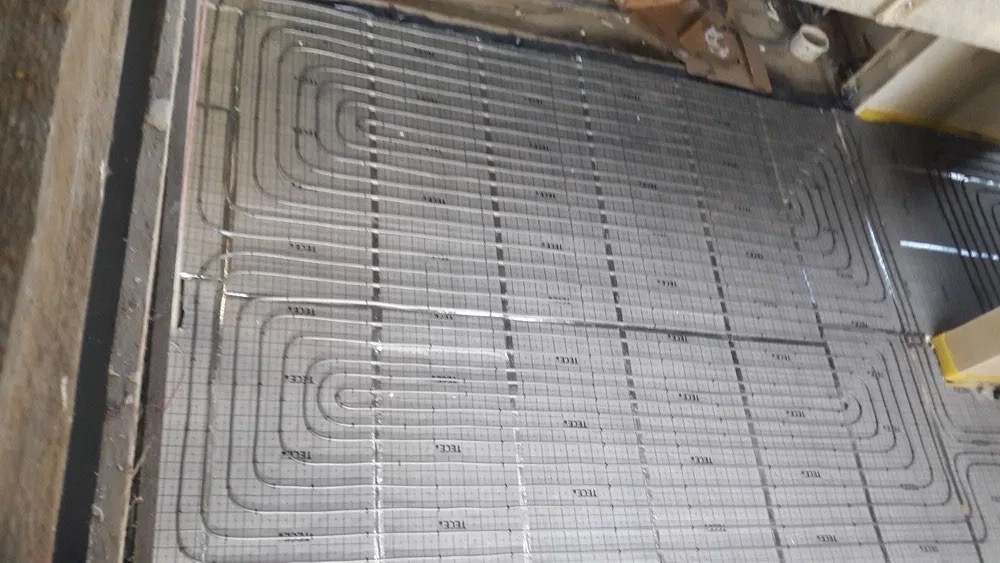 Instalacja rur systemu grzewczego podłogowego na izolacji z nadrukowaną siatką i oznaczeniami TECE, widok z góry, surowy stan przed wylewką.