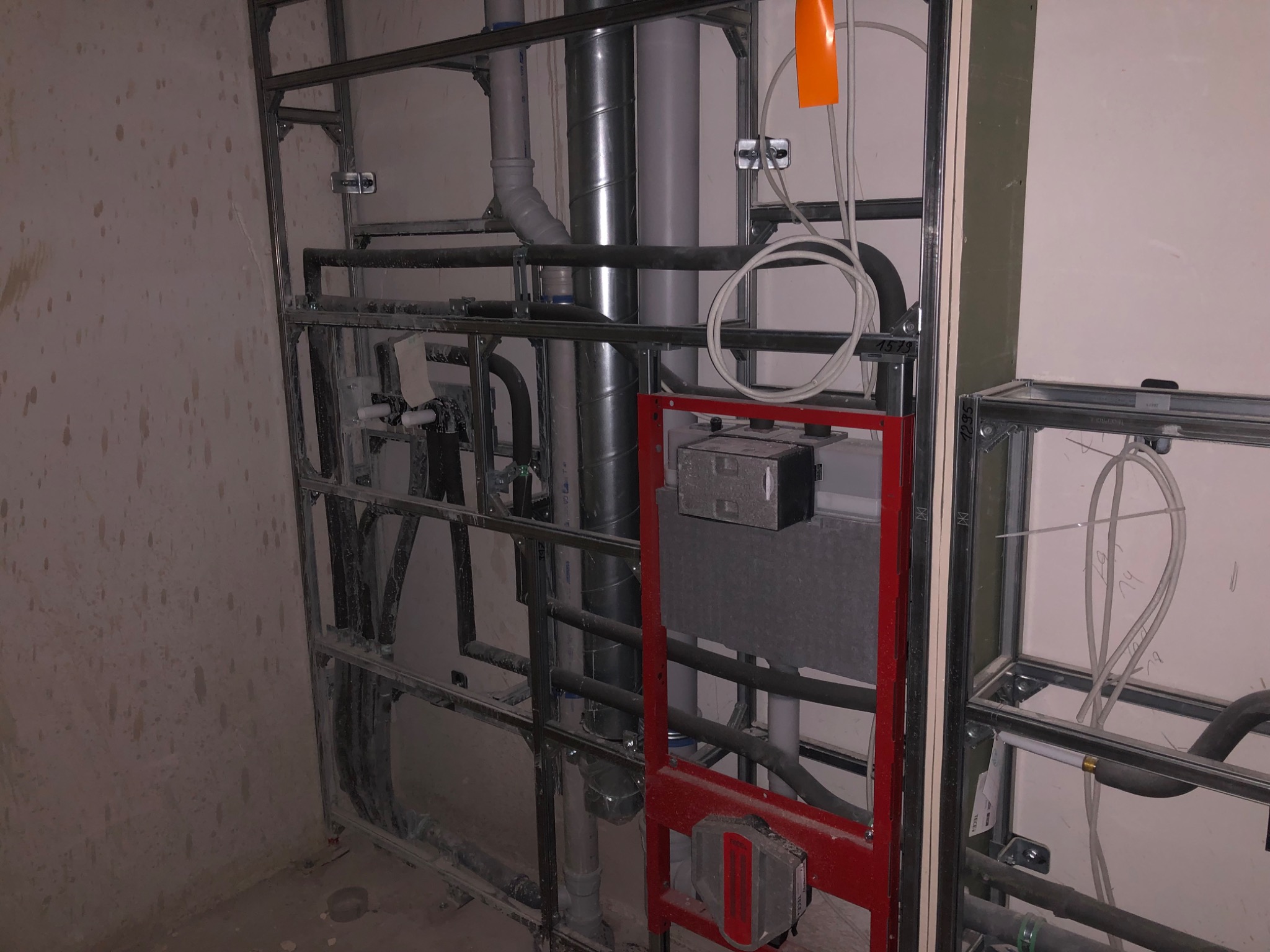 Stelaż instalacyjny podtynkowy z widocznymi rurami kanalizacyjnymi i wodnymi, zamontowany na ścianie w surowym stanie.